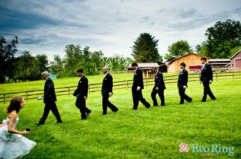 Groomsmen in a line while a flower girl runs in the opposite direction