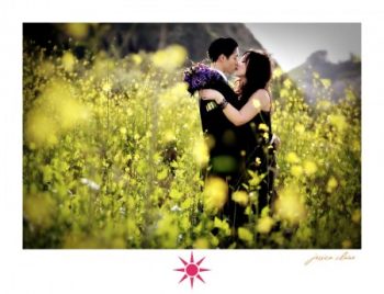 Newly weds dresses in black for an anniversary shoot kiss in a field while the bride holds a purple bouquet of flowers