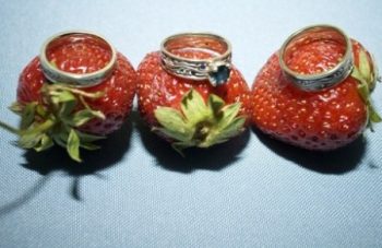 Three wedding rings on three whole strawberries