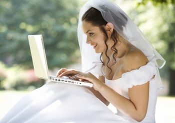Bride in wedding gown types on computer