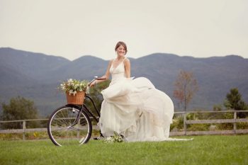 bride on bicycle in front of New Hampshire Mountains