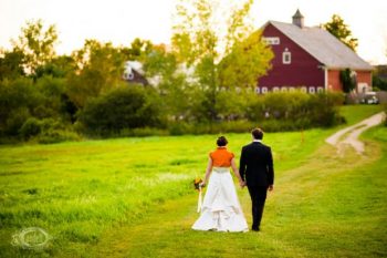 Bride in Orange Bolero walks to a red barn with Groom