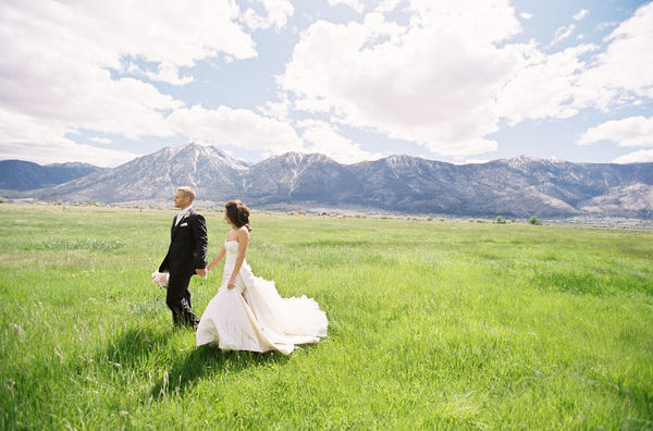 bride and groom walk across a meadow with mountains in the backgrond