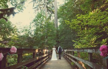 Camp wedding bride and groom cross a rustic wooden bridge