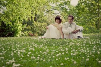 Hindsight Bride and Groom sit in afield of flowers