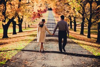 Couple walks down a tree-lined country road in autumn