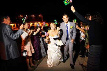 bride and groom exit while guests wave American and Brazilian Flags