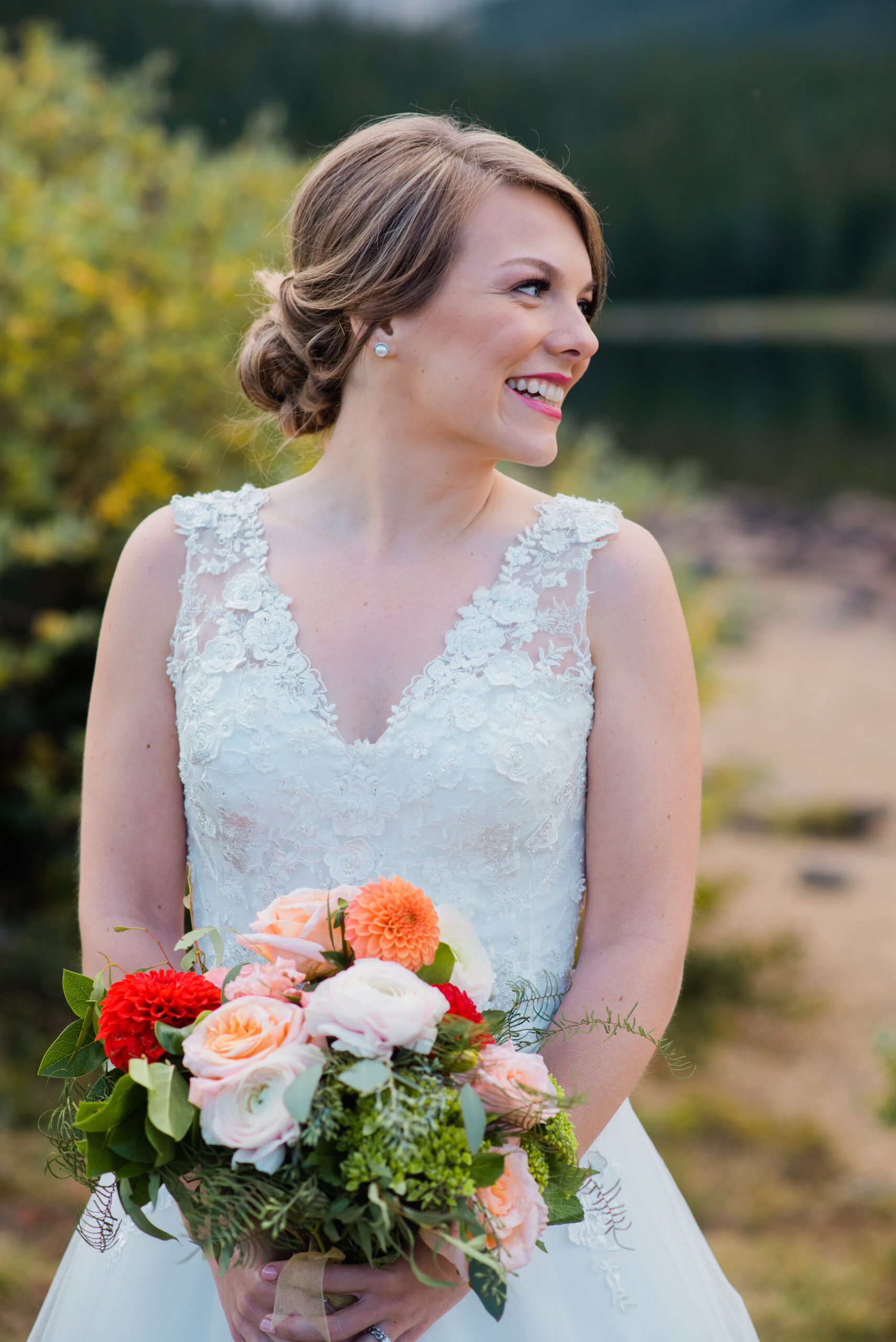 bride in lace wedding gown by the lake holding flowers