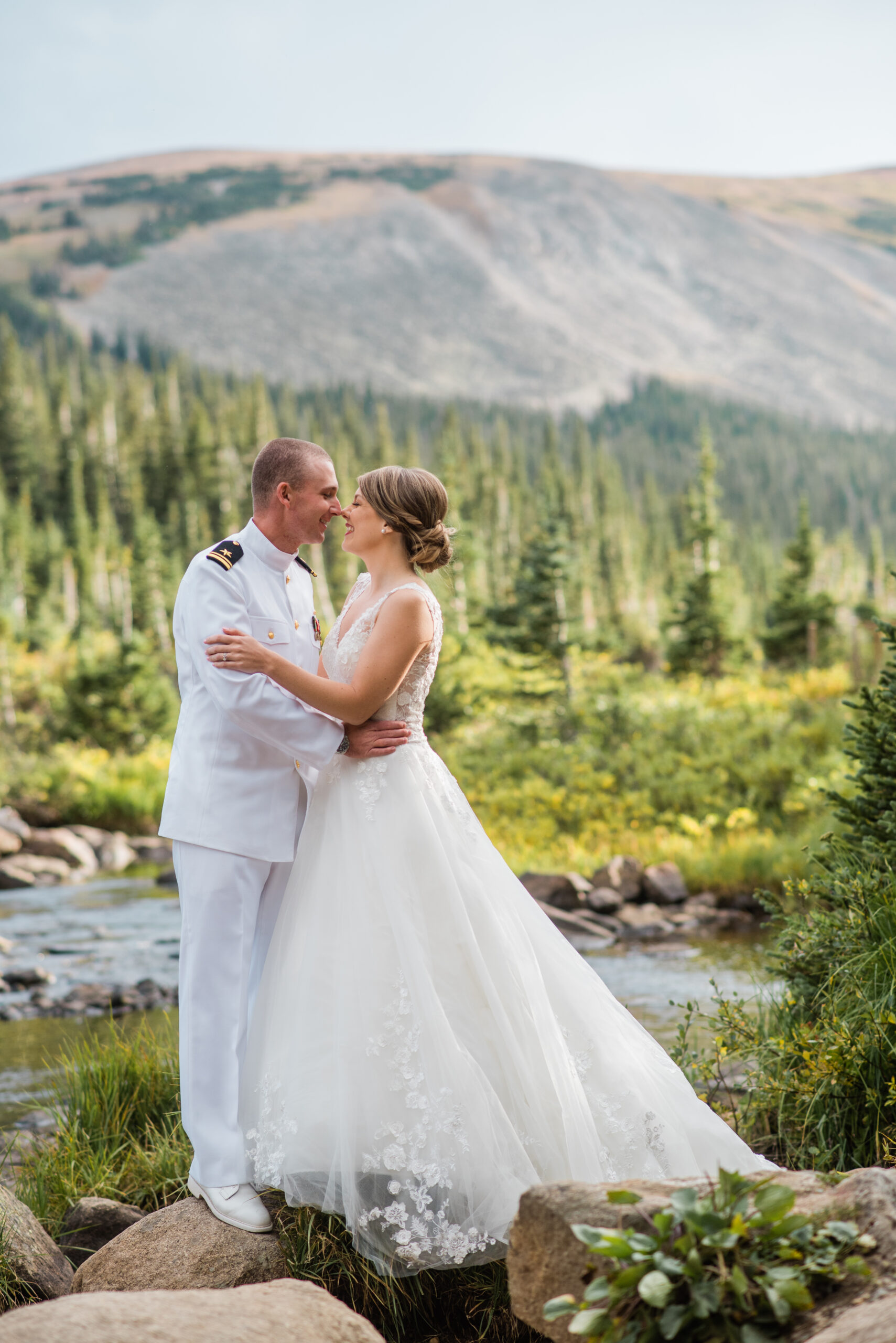bride and groom standing by lake with mountains in the background