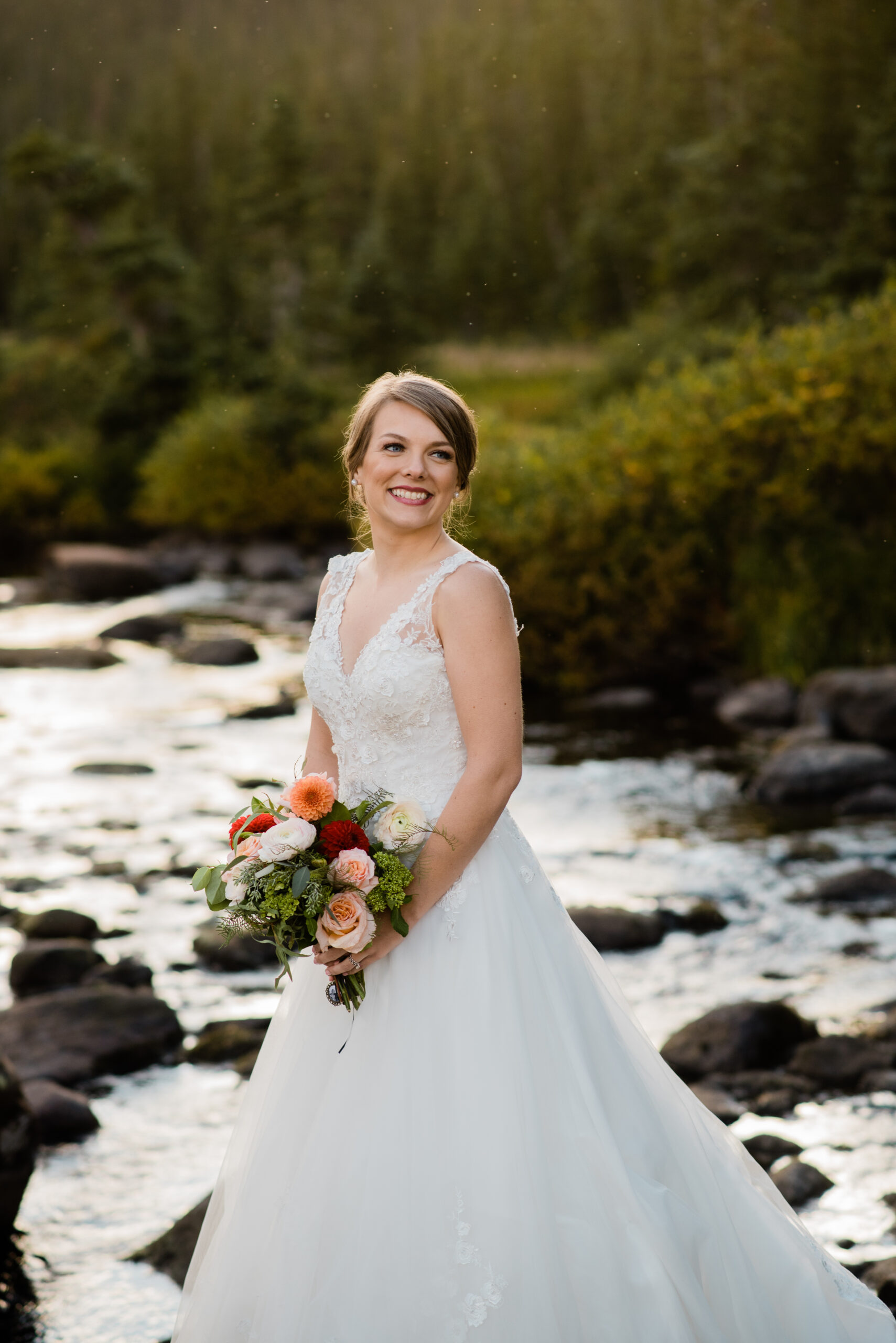 bride standing by lake with mountains in the background