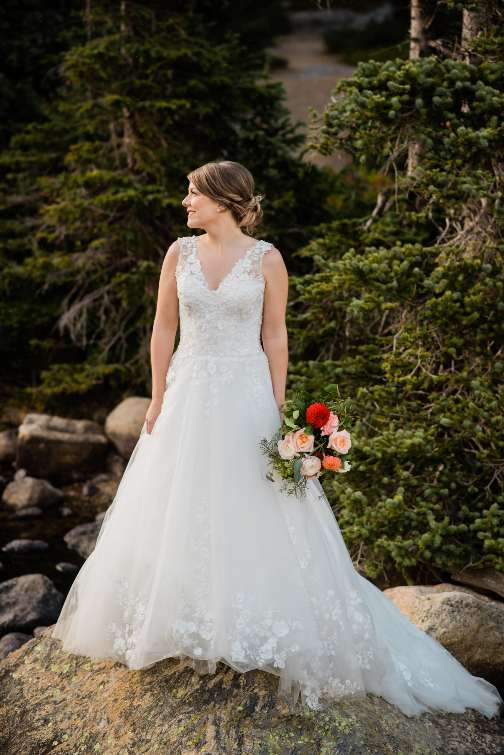 bride standing by lake with mountains in the background