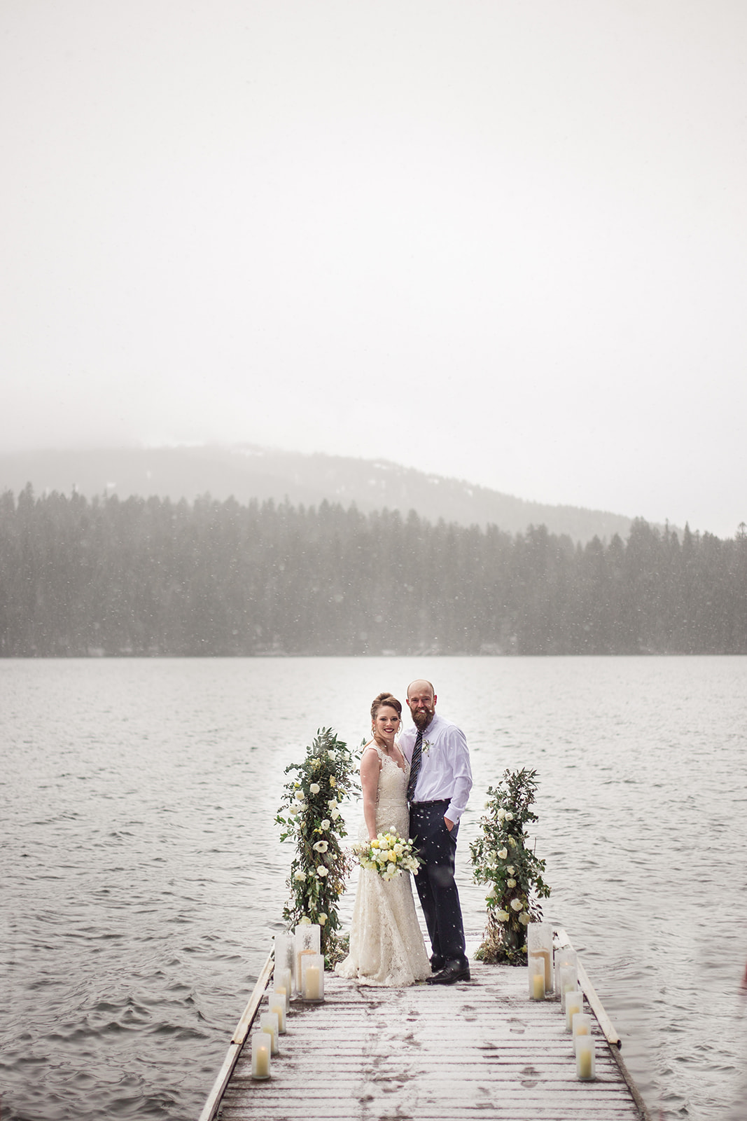 bride and groom on lake dock with mountains in the background