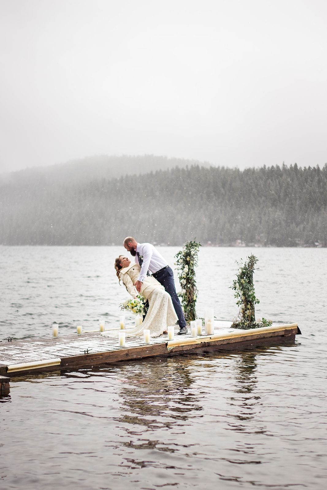 bride and groom on lake dock with mountains in the background