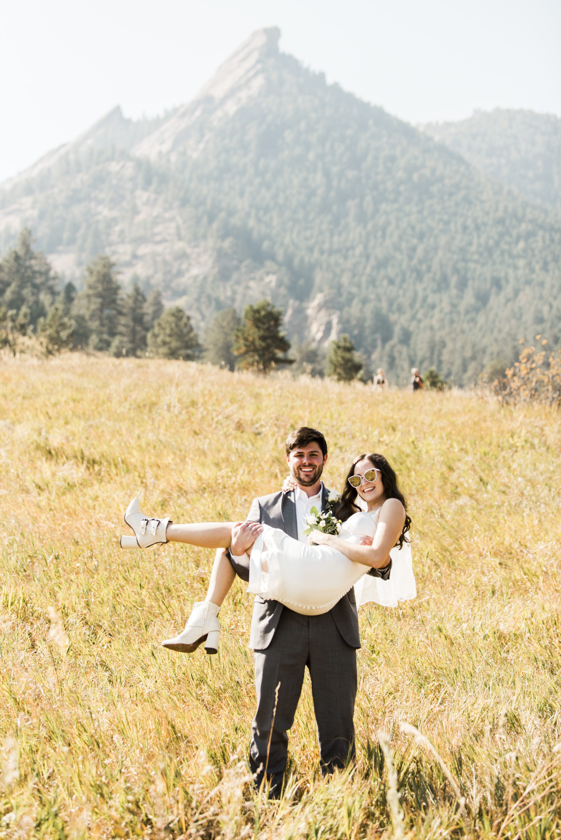 Bride in a short white dress and white boots carried by the groom in the Flatirons