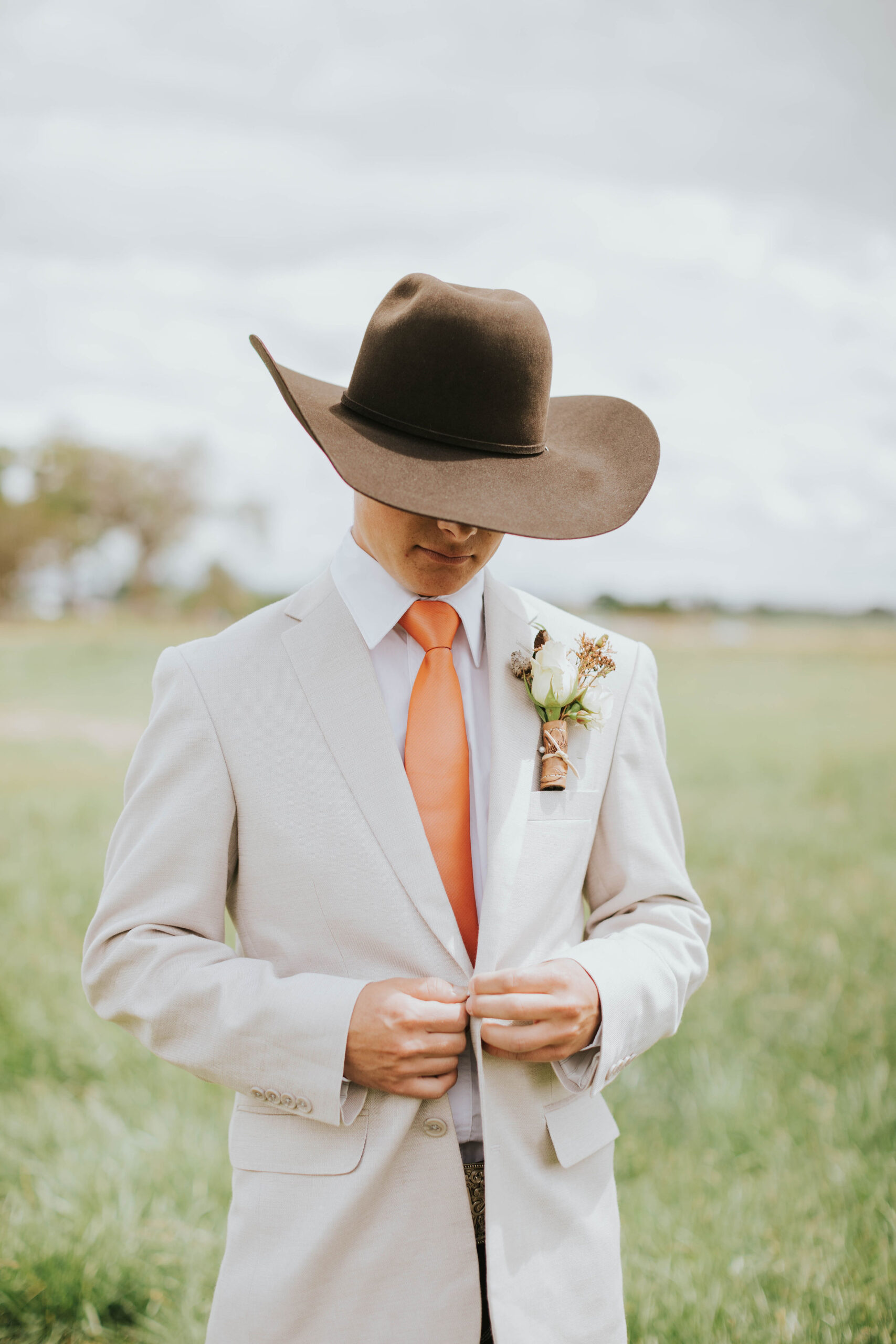 groom with light colored jacket, burnt orange tie, jeans and chocolate cowboy hat