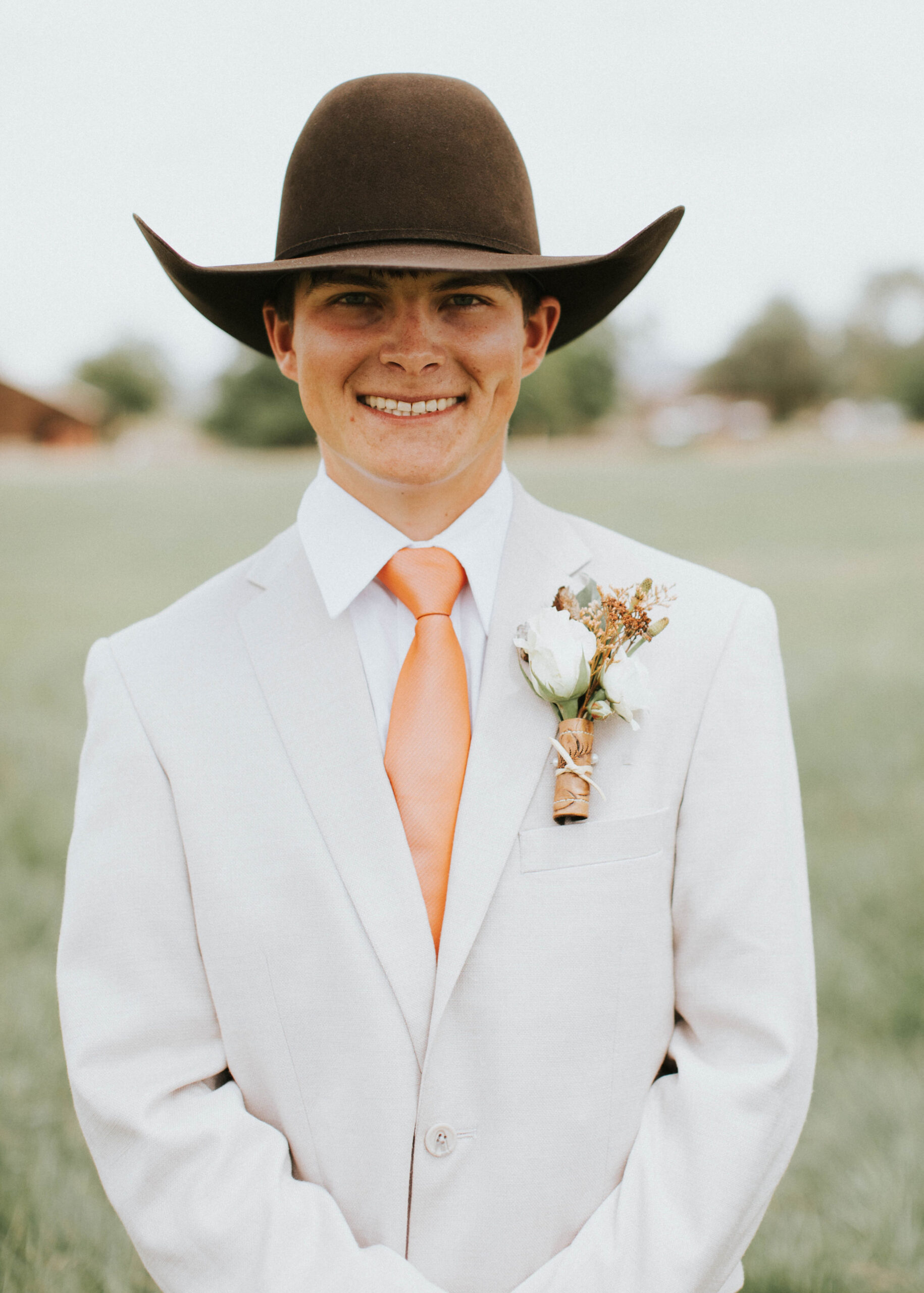 groom with light colored jacket, burnt orange tie, jeans and chocolate cowboy hat