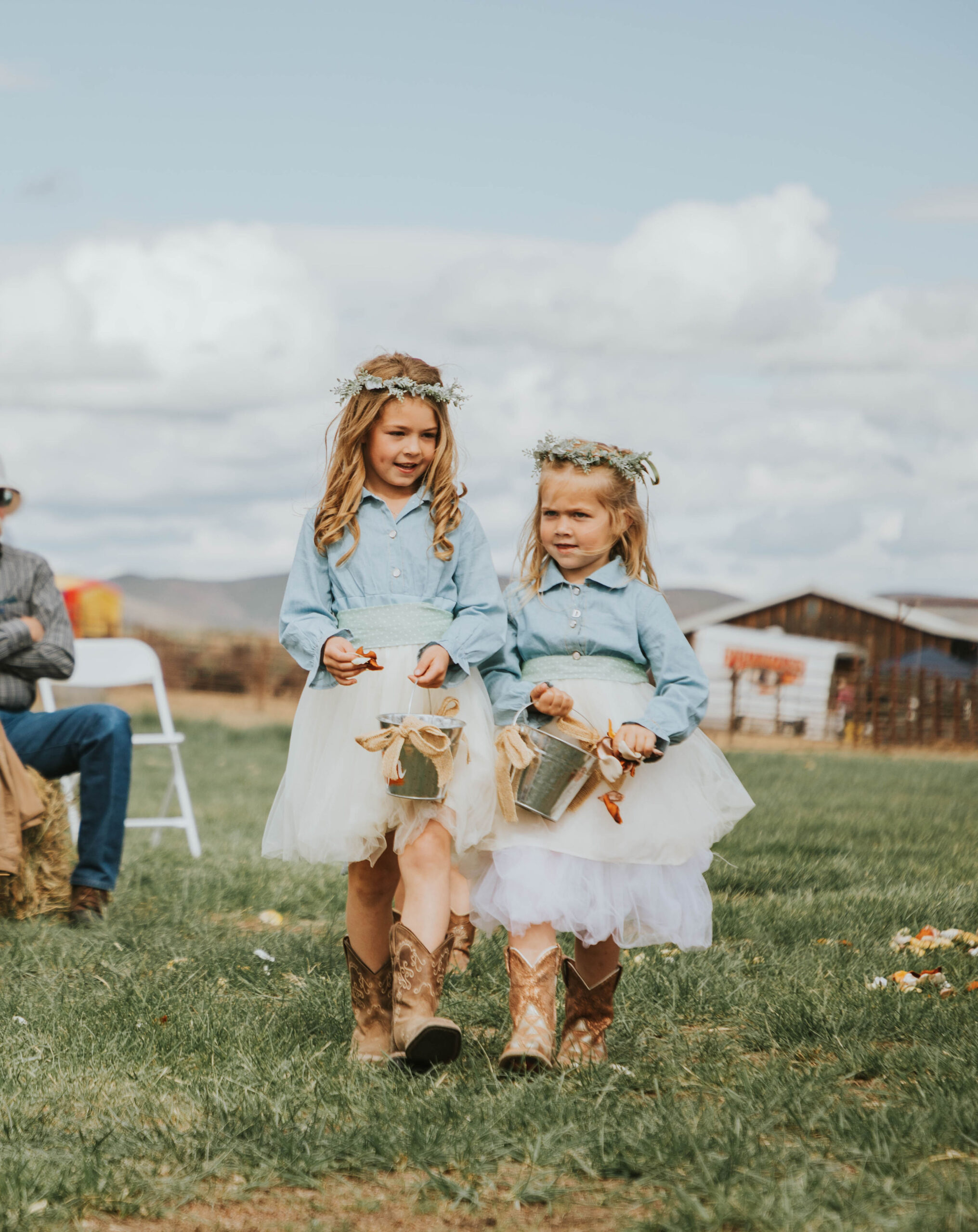 flower girls in jean shirts, tulle skirts and cowboy boots walking down aisle dropping flowers