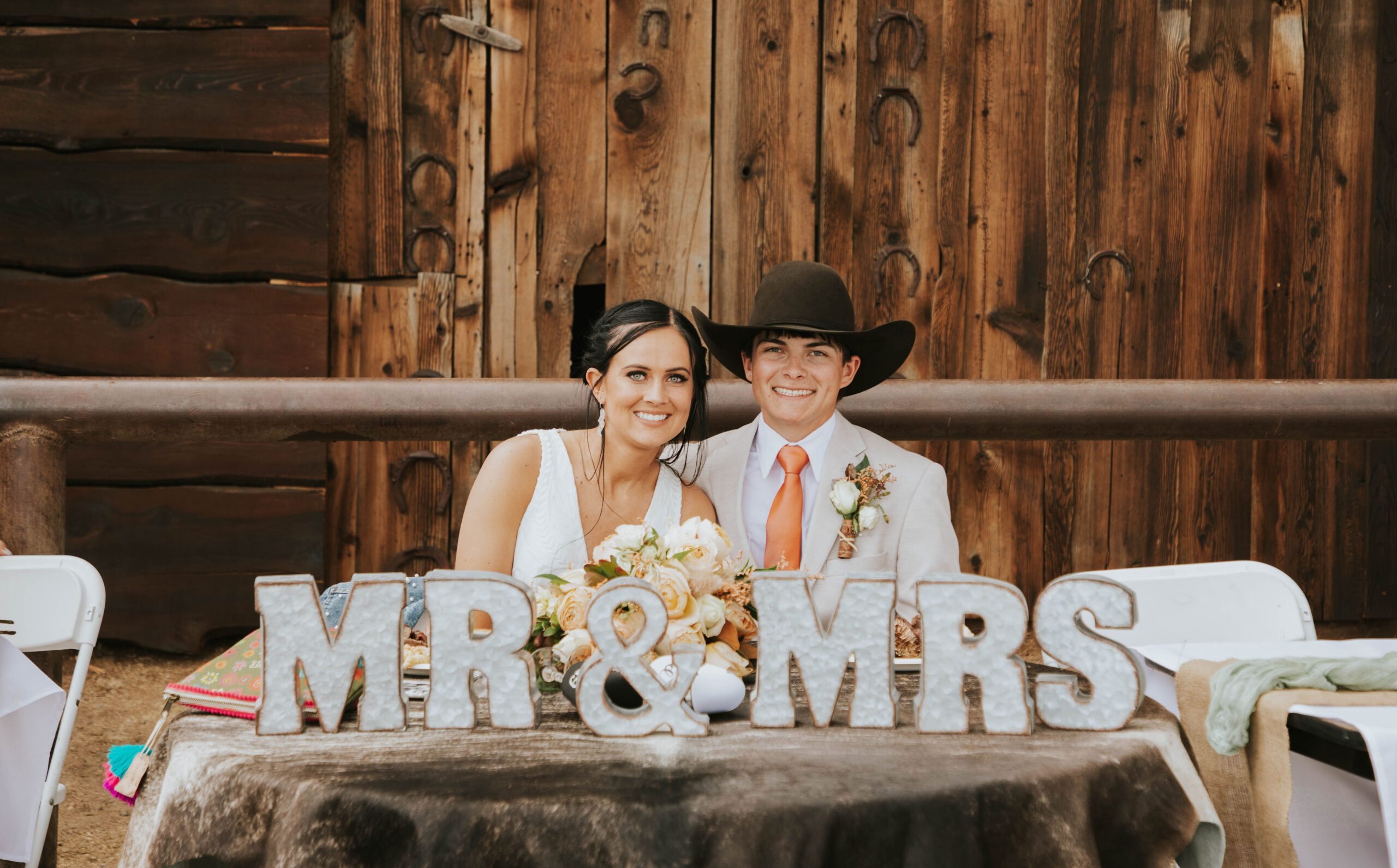 bride and groom setting at their couple's table with mr and mrs letters in a rustic orange mountain wedding
